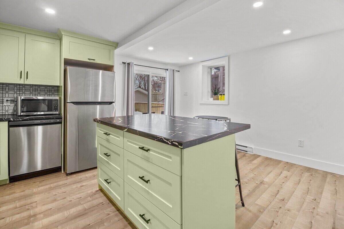 A kitchen with a large island, stainless steel appliances, and light green cabinets.