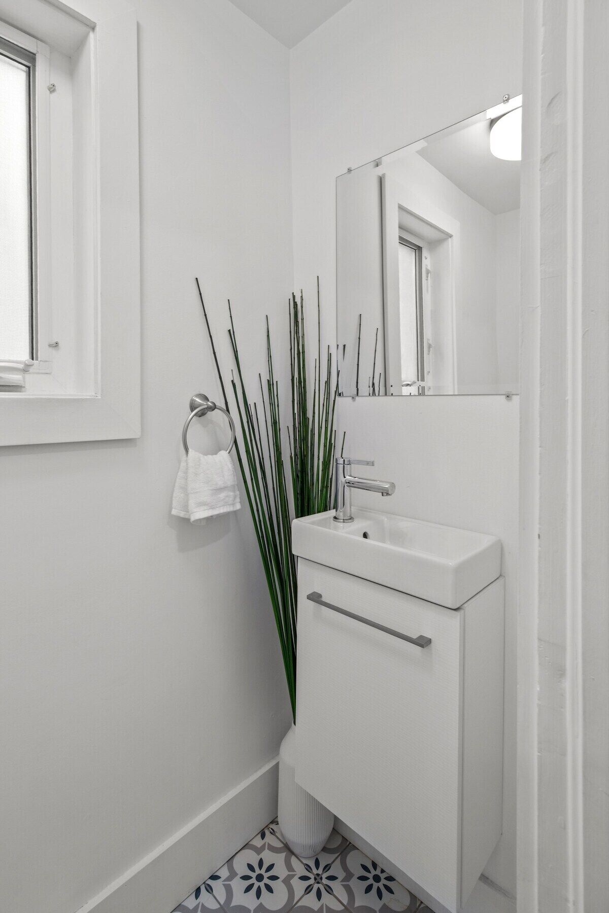 Une petite salle de bain blanche, avec un seul lavabo, un miroir et une fenêtre.