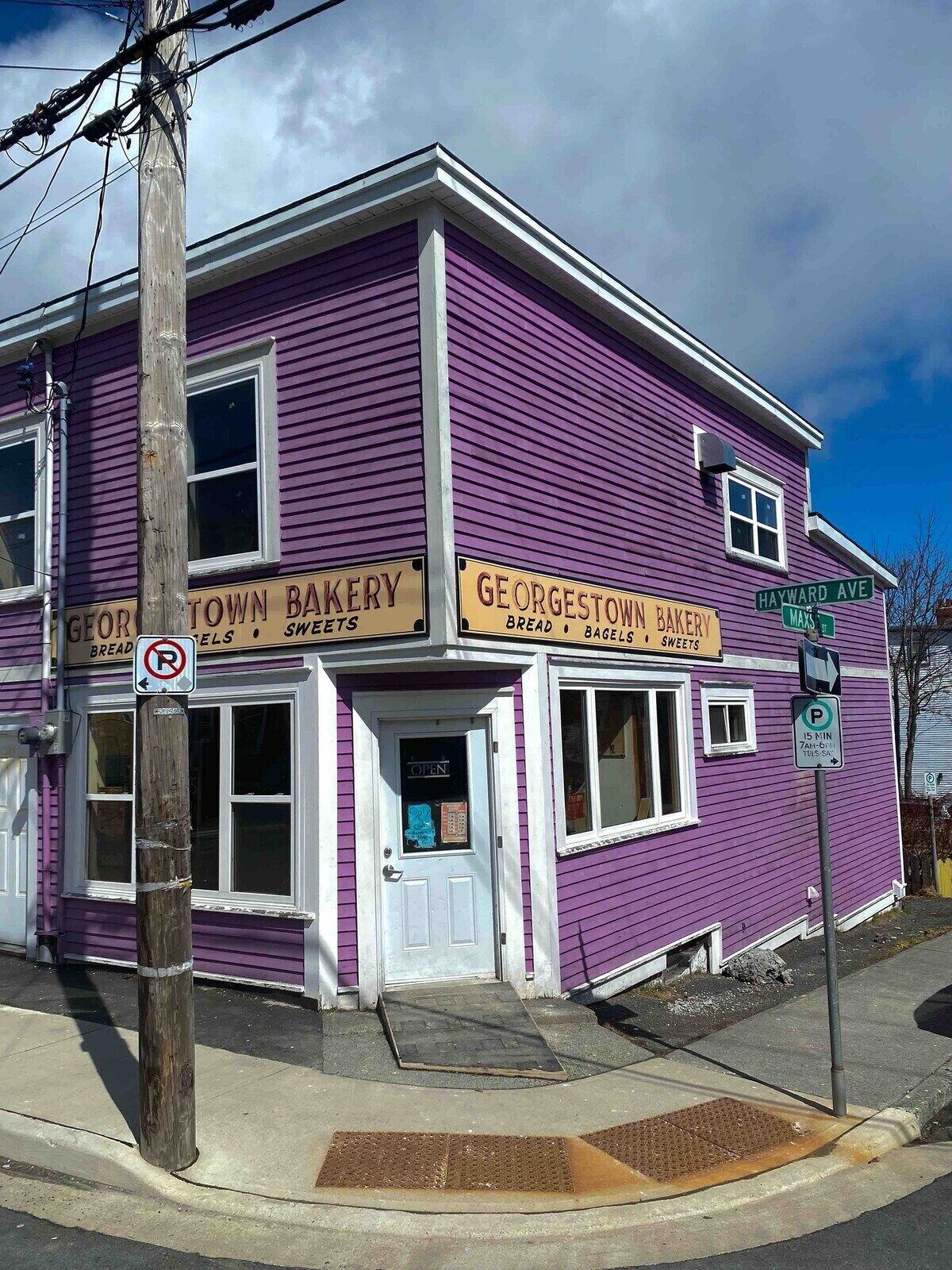 Un edificio morado con letreros que dicen 'Georgetown Bakery' y 'Town Bakery' en la planta baja, y 'Hayward Ave' en la esquina.