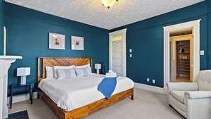 A bedroom with a wooden bed, white bedding, a blue throw, a white armchair, and a white door leading to a closet. - Victorian 4BR 2.5BA 2Parking Near Parks & DT (St. John's)