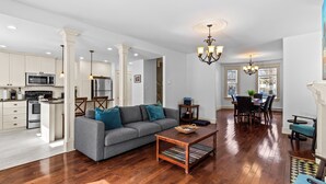 A spacious living area with a sofa, coffee table, dining table, and kitchen in the background. - Victorian 4BR 2.5BA 2Parking Near Parks & DT (St. John's)