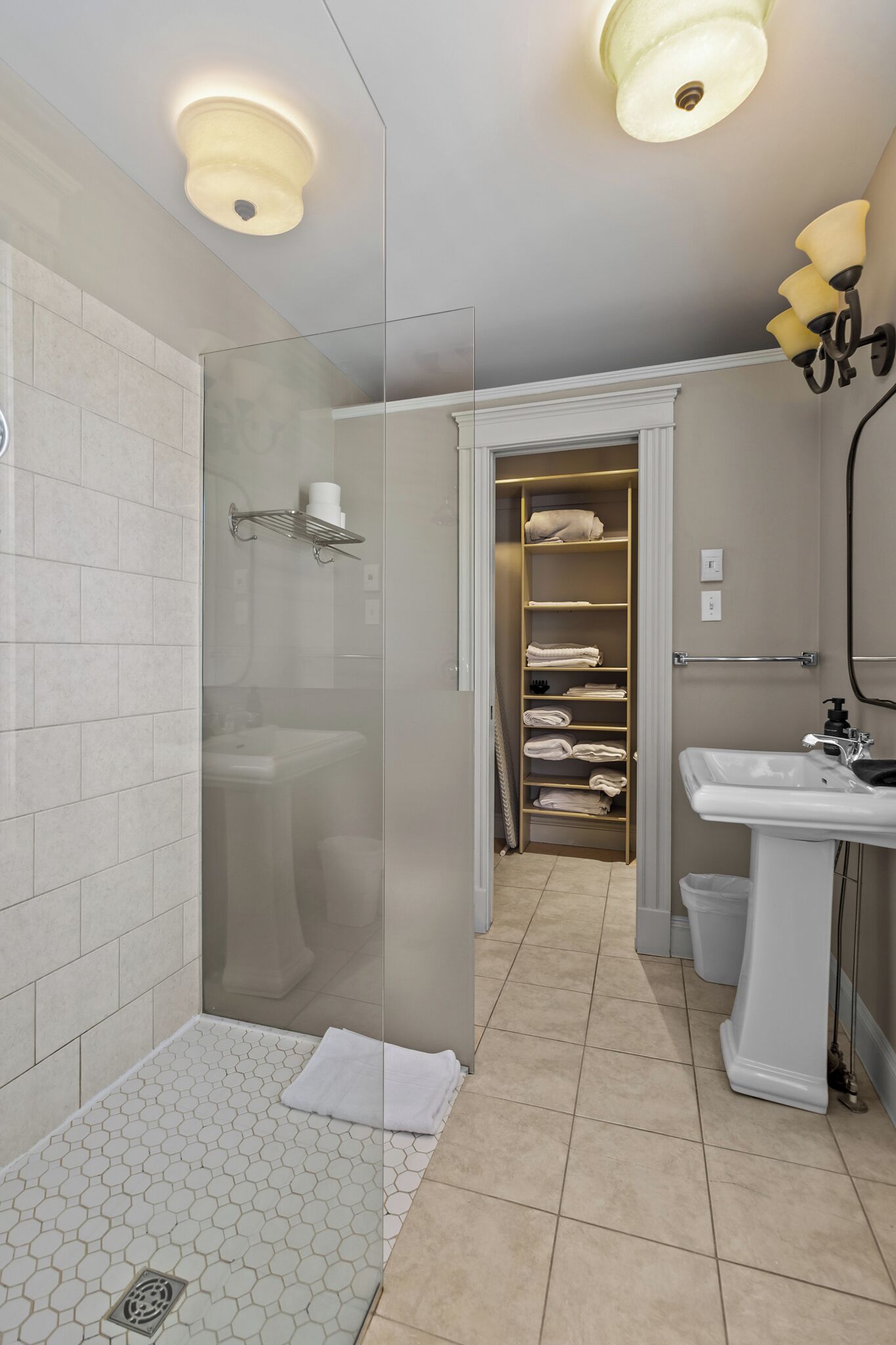 A modern bathroom with a glass shower enclosure, a white sink, and a storage closet with neatly folded towels.