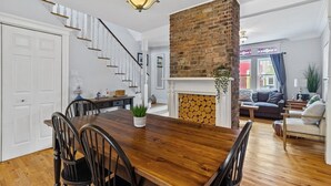 Un espace repas comprenant une table et des chaises en bois, une cheminée en briques et un escalier menant à un autre niveau.