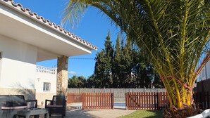 Zona de pati amb seients blanqus de relaxació, un pilaret de pedra i una tanca de fusta.