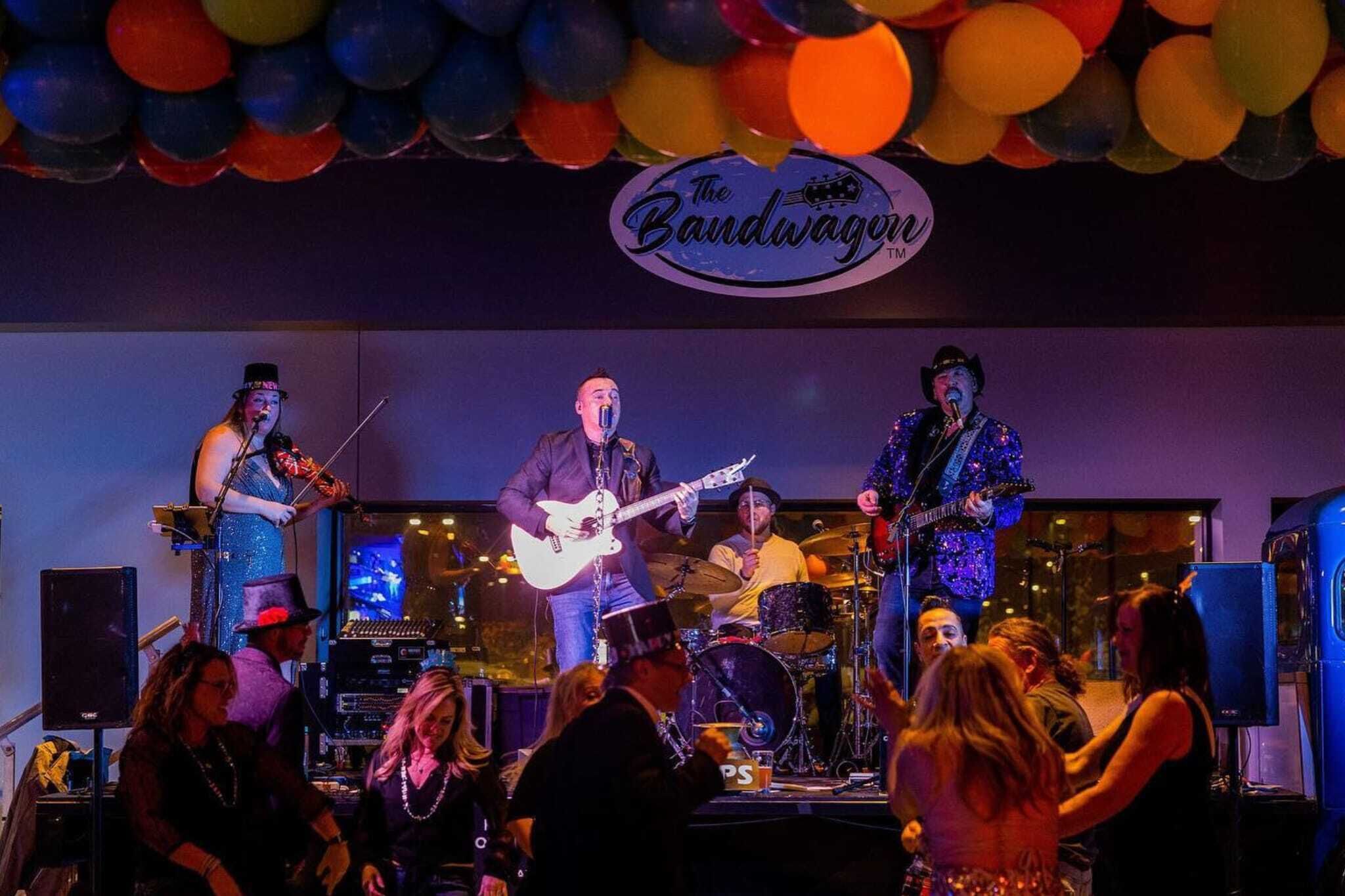A band performing on stage with a sign that reads "The Bandwagon."