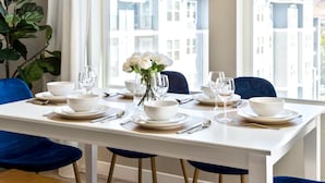 Une table à manger dressée avec des bols, des assiettes et des couverts blancs, et un vase rempli de fleurs blanches placé au centre.