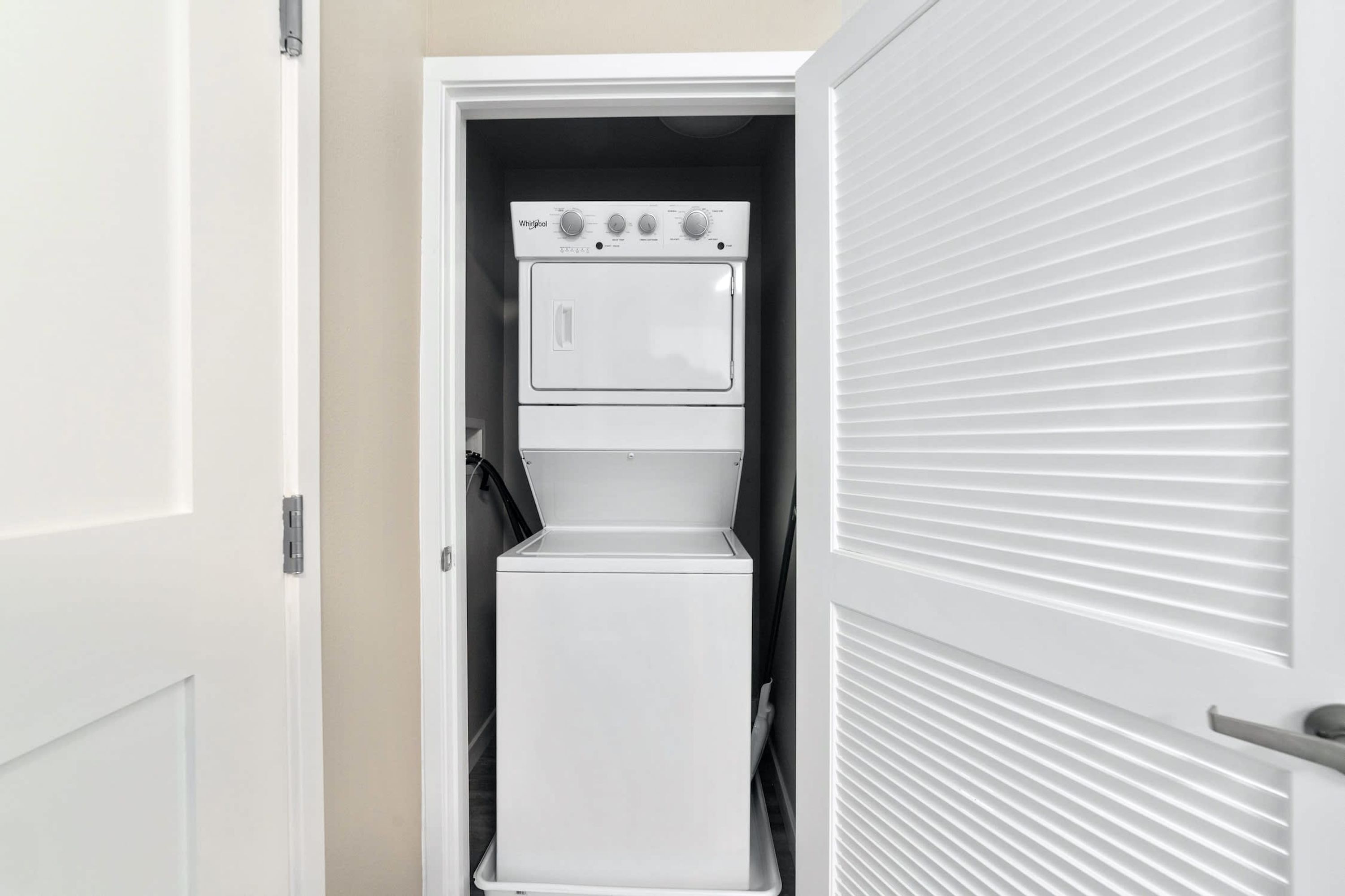 A compact, white laundry room with a built-in washer and dryer, a small shelf, and a door with a handle.