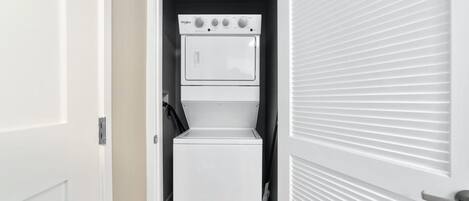 A compact, white laundry room with a built-in washer and dryer, a small shelf, and a door with a handle.