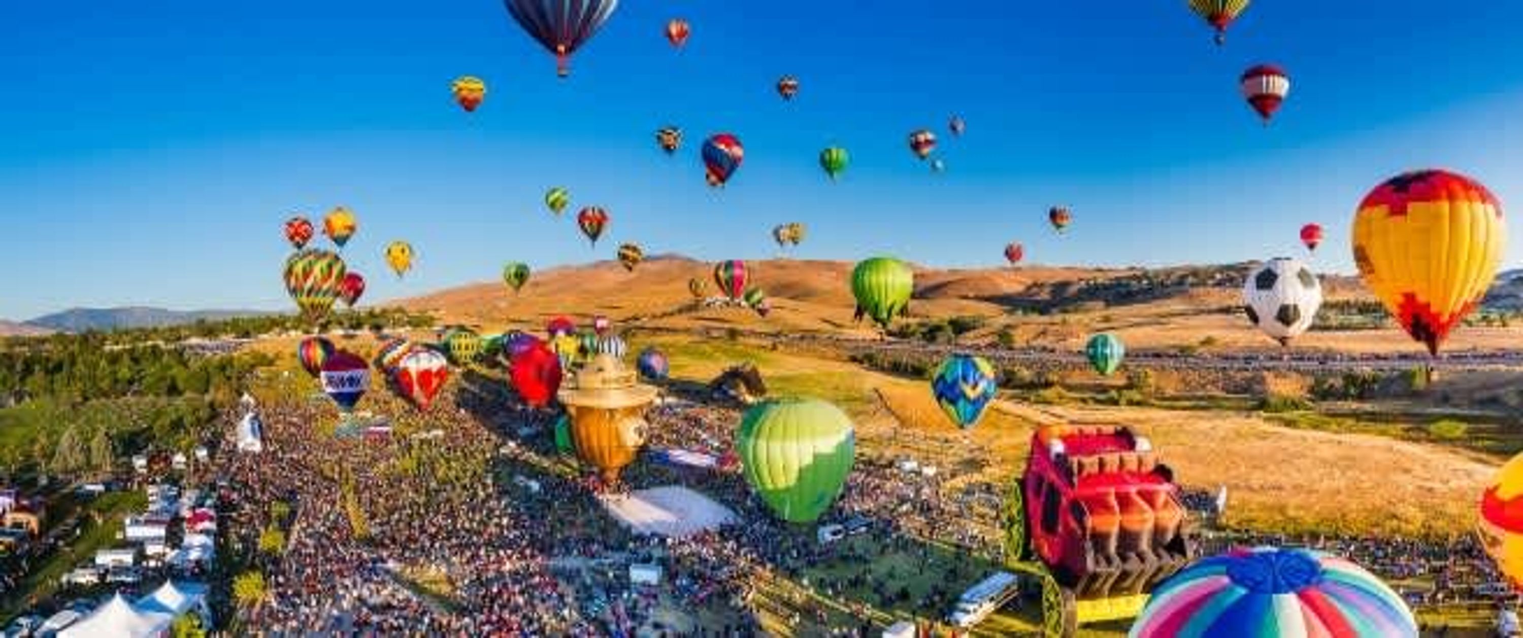 A hot air balloon festival with numerous colorful balloons in the sky and a large crowd on the ground.