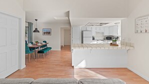 A modern kitchen with white cabinets, a central island, and a dining area with teal chairs and a wooden table. - Delightful 4BR Home Nr Downtown Reno w Fireplace (Reno)