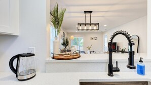 Una cocina moderna con encimera blanca, hervidor negro, lavamanos y un original grifo negro.