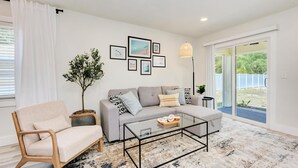 Un salón moderno con un sofá gris, un sillón color beige, una mesa de centro de cristal y una planta en maceta.