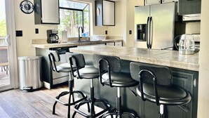 Une cuisine moderne dotée d’un îlot central, de tabourets de bar, d’appareils électroménagers en acier inoxydable et d’une horloge murale.