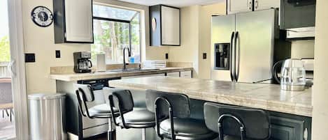 A modern kitchen with a central island, bar stools, stainless steel appliances, and a clock on the wall.
