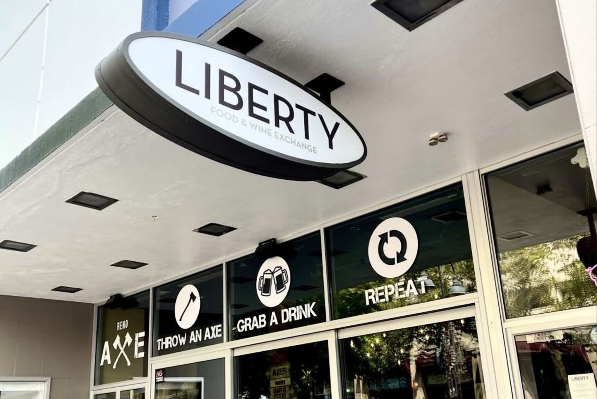 Fachada con un letrero que dice "LIBERTY FOOD & WINE EXCHANGE" y tres ventanas con los rótulos "REPEAT", "GRAB A DRINK" y "THROW AN AXE".