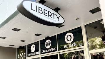 Fachada con un letrero que dice "LIBERTY FOOD & WINE EXCHANGE" y tres ventanas con los rótulos "REPEAT", "GRAB A DRINK" y "THROW AN AXE".