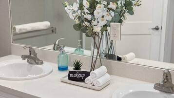 Un bagno con due lavandini, un ampio specchio e un vaso con fiori bianchi.
