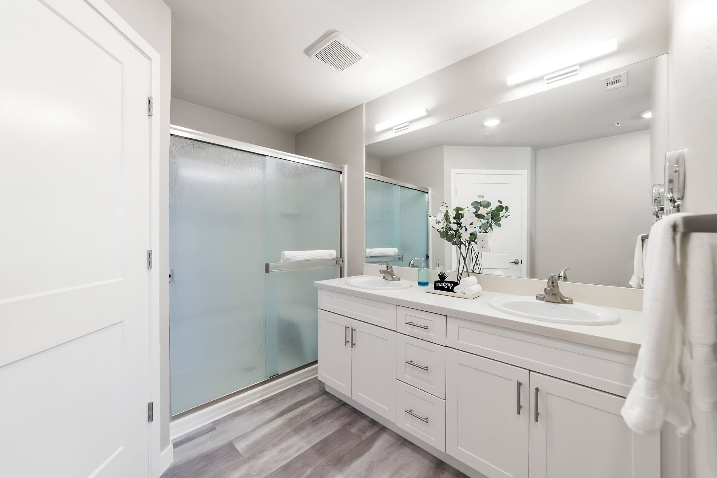 A modern bathroom with a glass shower enclosure, white vanity with a sink, and a large mirror.