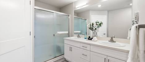 A modern bathroom with a glass shower enclosure, white vanity with a sink, and a large mirror.