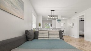 A modern living room with a sofa, a coffee table, and a dining area with a chandelier. - Relaxing 2BR Florida Home Close to Beach (Osprey)
