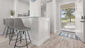 A modern kitchen with a white island, bar stools, and a clock on the wall. - Relaxing 2BR Florida Home Close to Beach (Osprey)