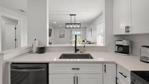 A modern kitchen with white cabinetry, a stainless steel sink, a coffee maker, and a dishwasher. - Relaxing 2BR Florida Home Close to Beach (Osprey)