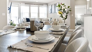 Uma sala de jantar com uma mesa comprida posta para refeição, cadeiras e um vaso com flores.