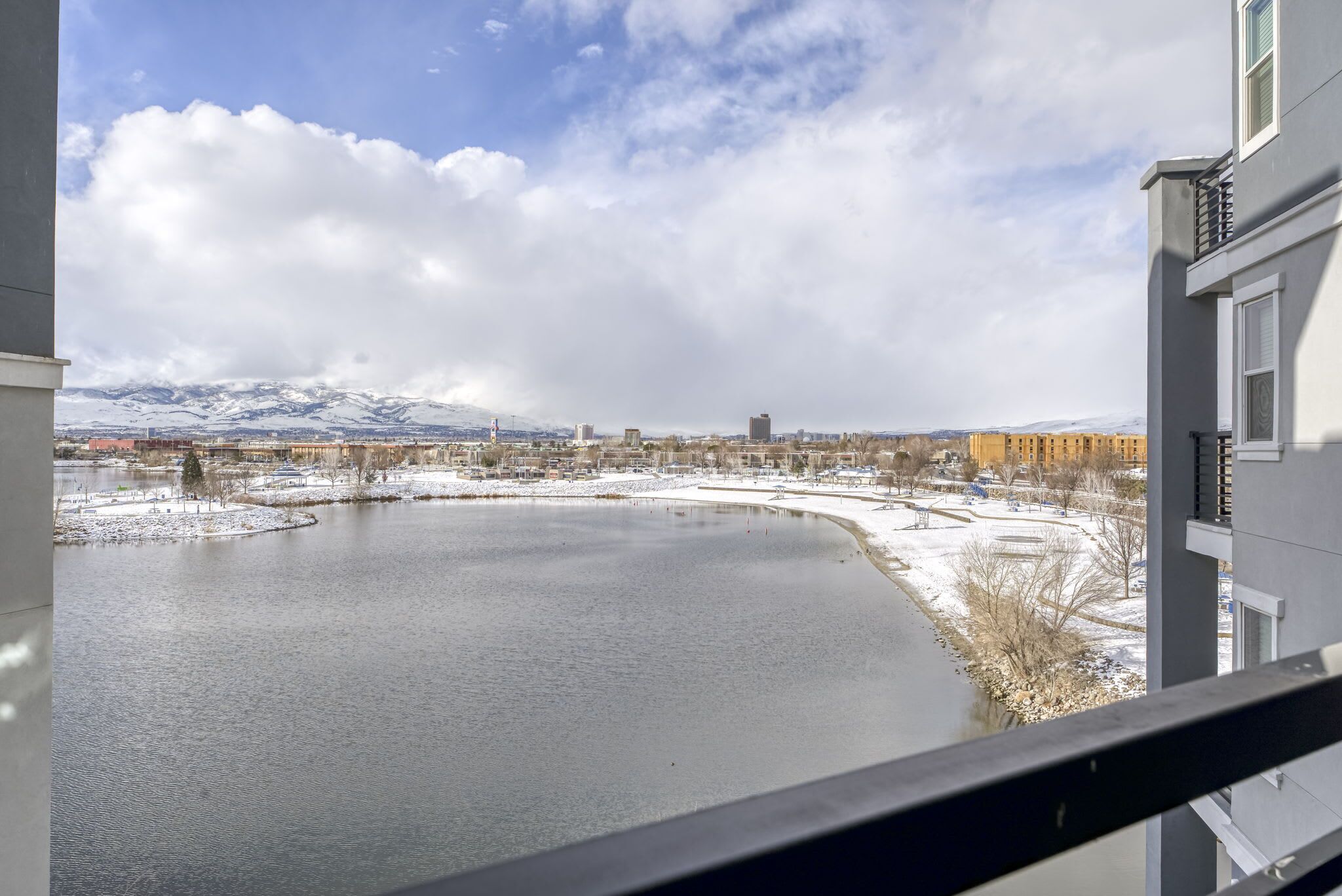 A view of a lake with snow-covered mountains in the background, surrounded by buildings.