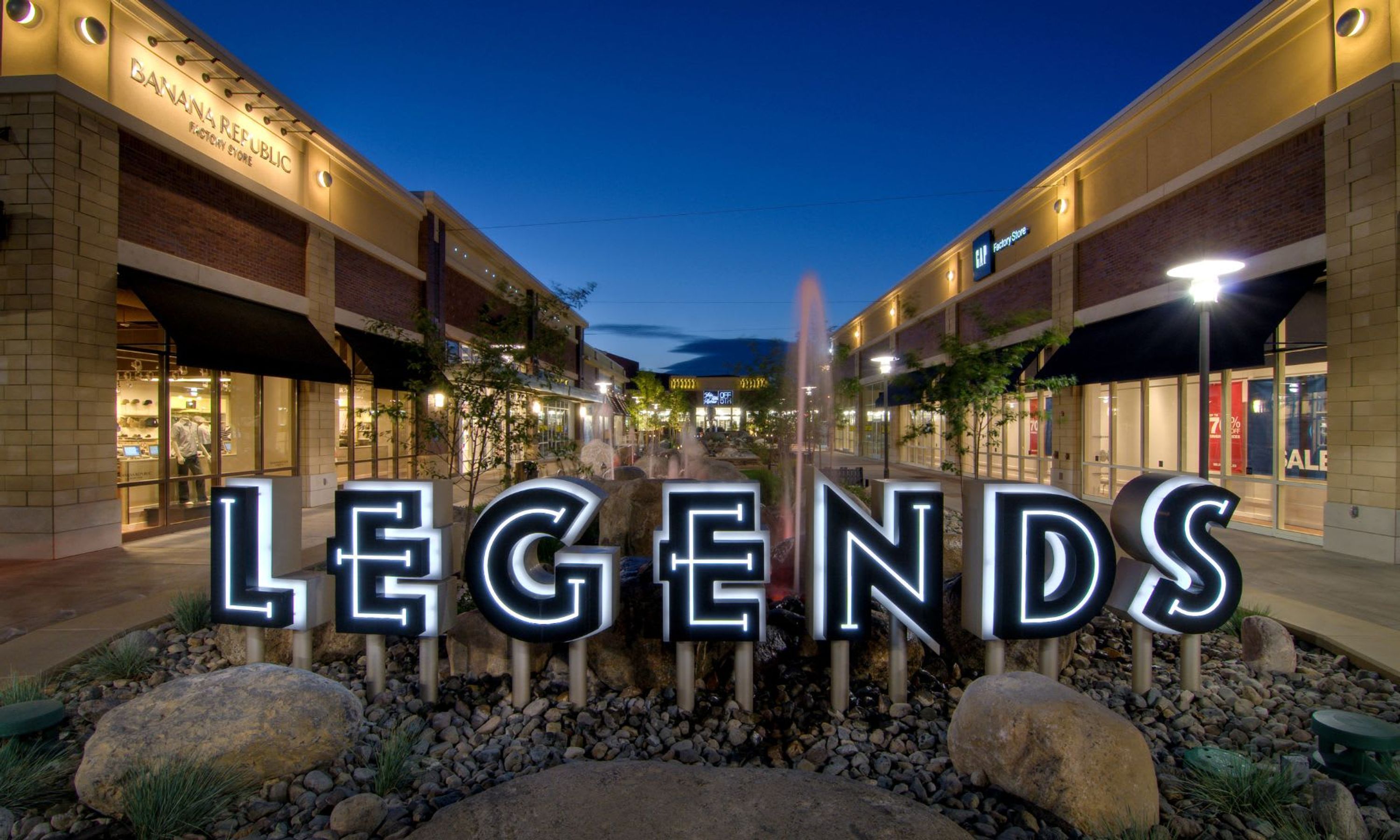 Zona comercial con escaparates iluminados y un llamativo letrero que dice 'LEGENDS'.