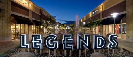 Zona comercial con escaparates iluminados y un llamativo letrero que dice 'LEGENDS'.