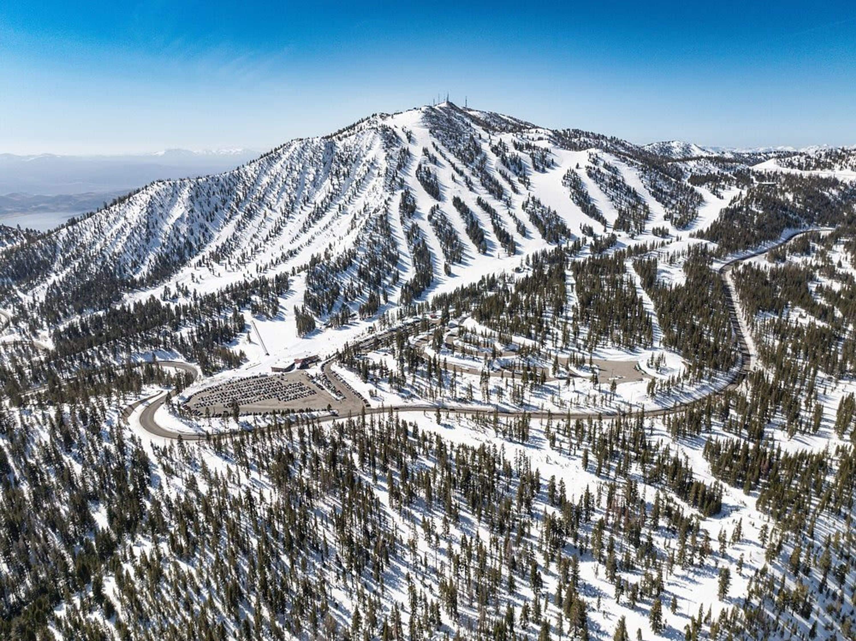 Une montagne enneigée abritant une station de ski, avec des pistes et un parking.
