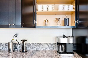 A kitchen with a coffee maker, a kettle, and a cabinet with white cups and a coffee grinder. - Stylish Sleek 4BR Nevada Home Near Downtown Reno (Sparks)