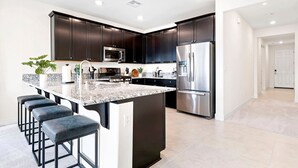 A modern kitchen with dark cabinets, stainless steel appliances, a granite countertop, and bar stools. - Stylish Sleek 4BR Nevada Home Near Downtown Reno (Sparks)
