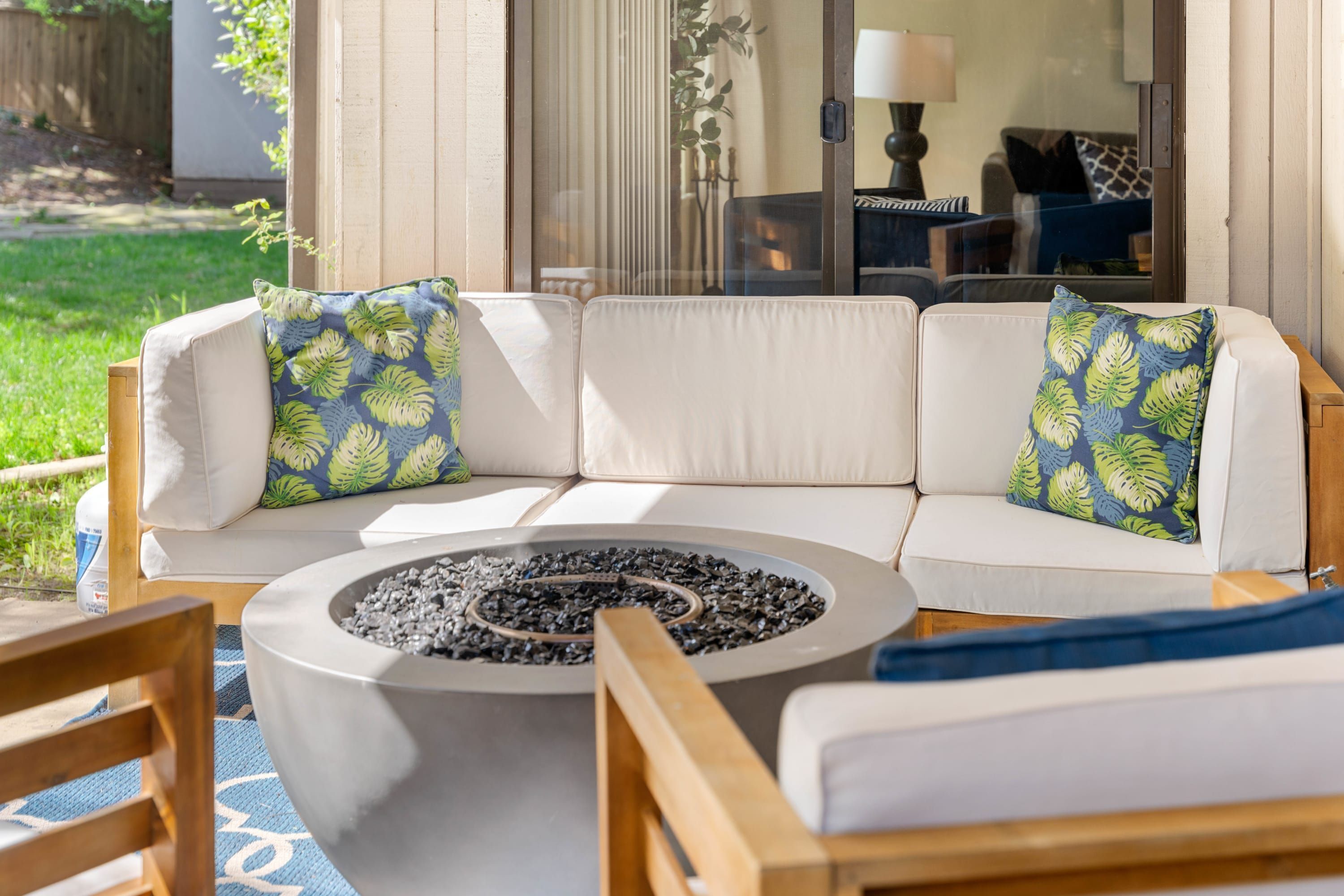 A modern outdoor seating area with a fire pit, white cushioned sofas, and patterned throw pillows.