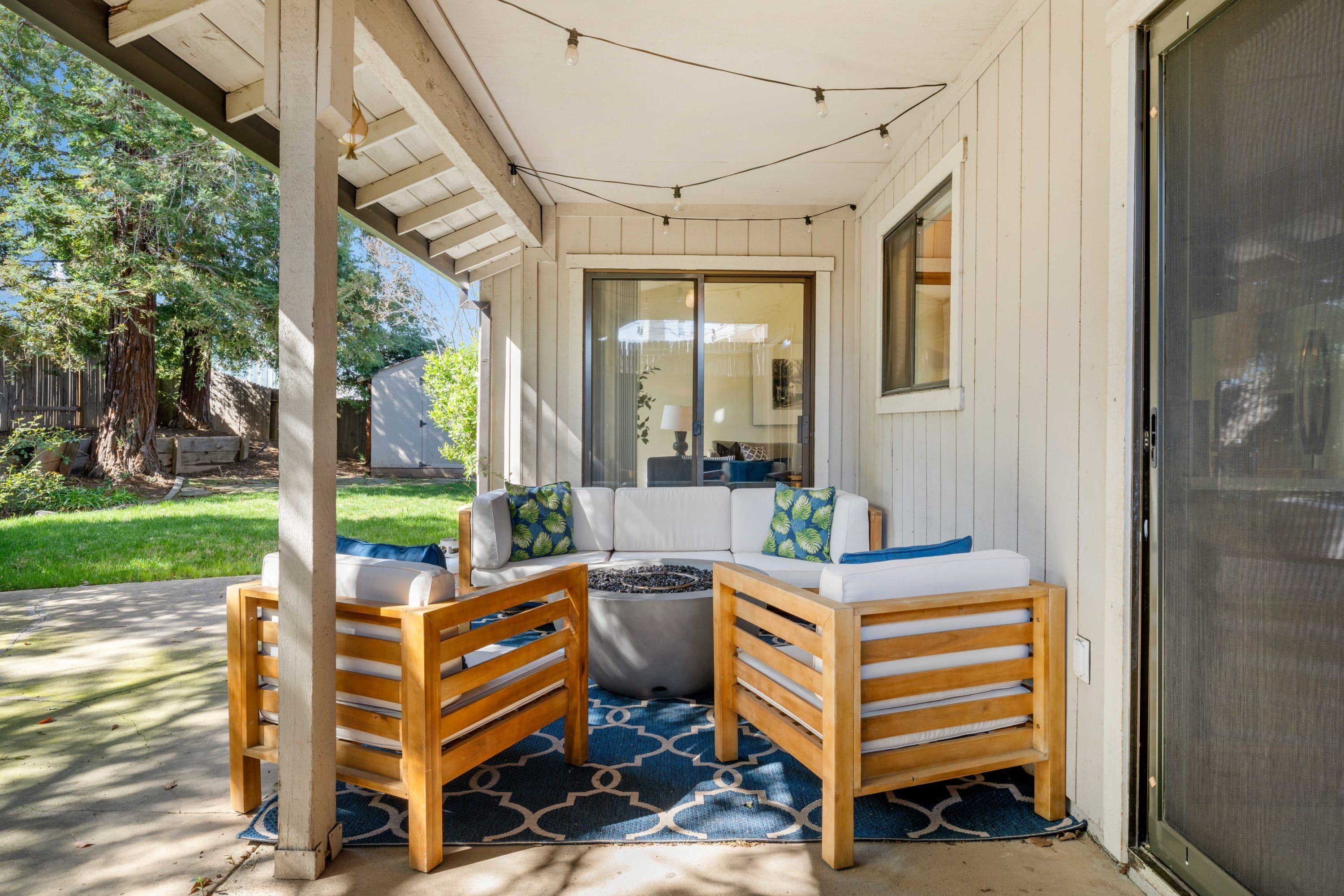 A covered patio with a seating area, a fire pit, and a sliding glass door.