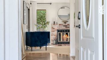 A hallway leading to a living room with a fireplace, a round mirror, and a blue sofa.