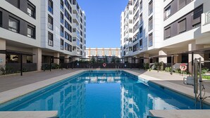 Una piscina rodeada de edificios modernos con balcones, cielos despejados y un flotador en el borde de la piscina.