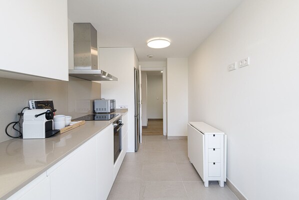 A narrow, well-lit kitchen with white cabinetry, a built-in microwave, and a Nespresso machine.