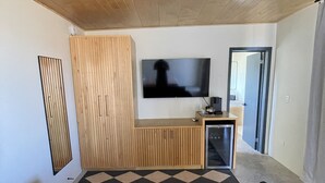 A modern living room with a wooden ceiling, a large flat-screen TV mounted on the wall, a built-in wooden entertainment unit, and a checkered floor rug. - MILU-CABAÑA SENCILLA (Guadalupe)
