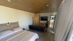 A modern hotel room with a large bed, a sofa, a TV, and a wooden ceiling. - MILU-CABAÑA SENCILLA (Guadalupe)