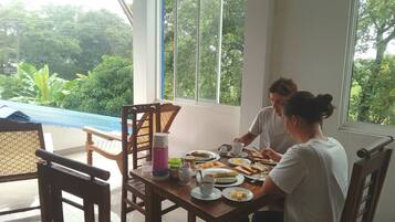 A dining area with a table set for two, surrounded by chairs, with a view of greenery outside.