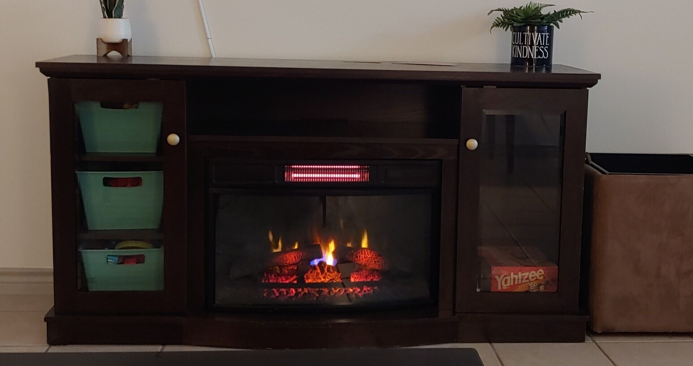 Una chimenea con frente de vidrio, un estante encima y contenedores de almacenamiento a la izquierda.