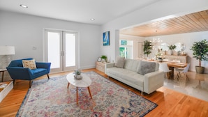 Ein modernes Wohnzimmer mit einem blauen Sessel, einem weißen Sofa, einem runden Couchtisch und einem farbenfrohen Teppich.
