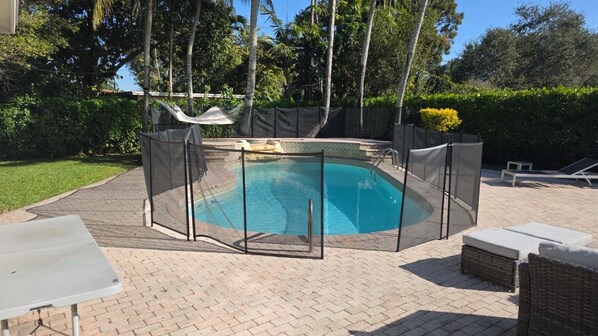 A swimming pool with a safety fence, surrounded by a brick patio, and equipped with lounge chairs and a table. - Miami Home - Private Pool  - We Host (Miami)