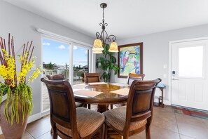 A dining area with a round glass table, wooden chairs, a hanging light fixture, and a large window with a view.