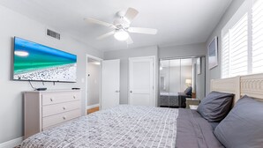 Ein Schlafzimmer mit einem Bett, einem Deckenventilator, einem an der Wand befestigten Fernseher und einer Tür zu einem anderen Raum.