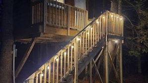 Une cabane en bois avec un escalier et un balcon, entourée d’arbres.