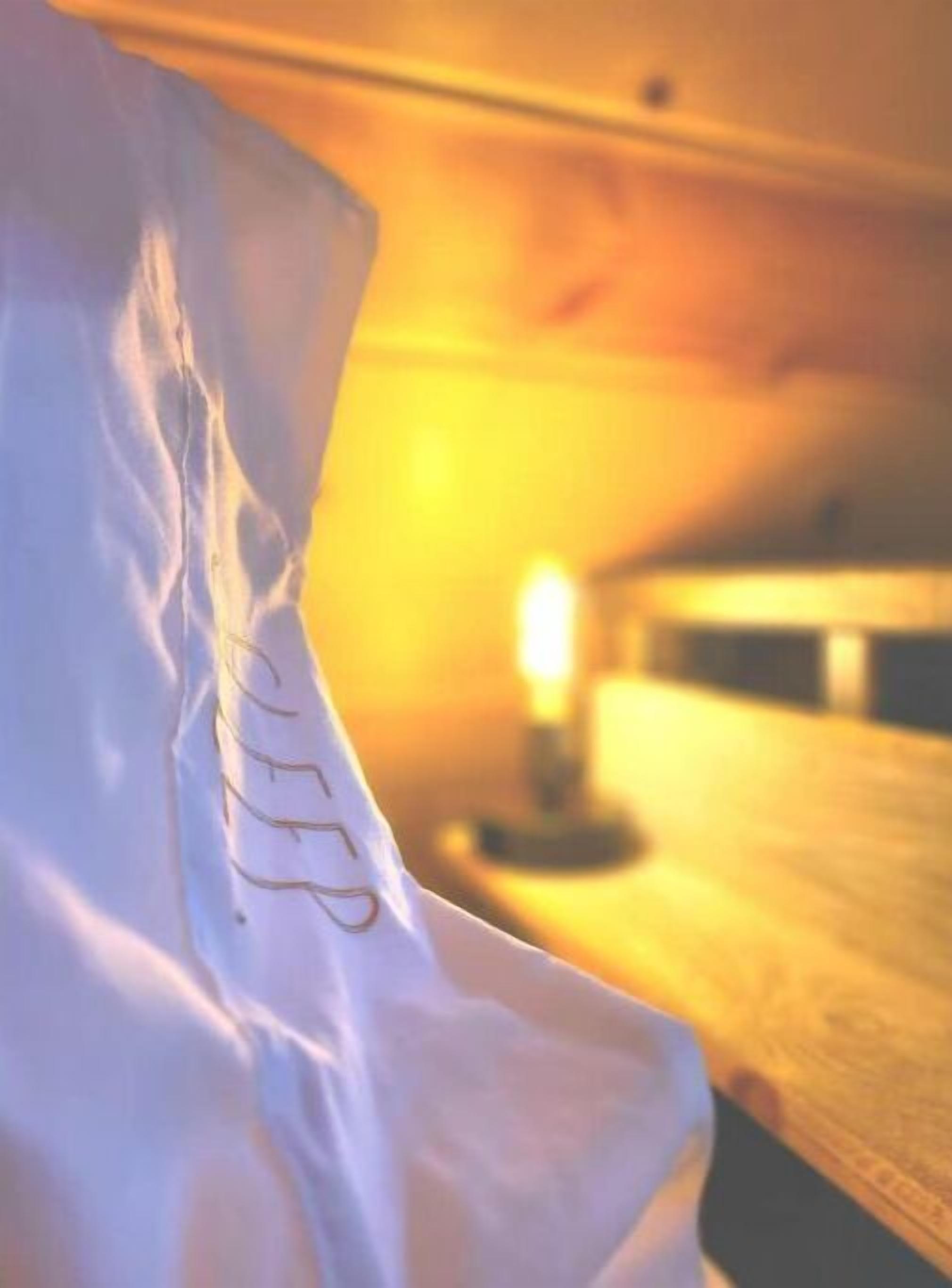 A white pillow with a visible text pattern, a wooden surface, and a blurred light source in the background.