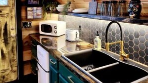 Une cuisine avec un plafond en bois, un four à micro-ondes, un grille-pain, un évier et un téléviseur fixé au mur.