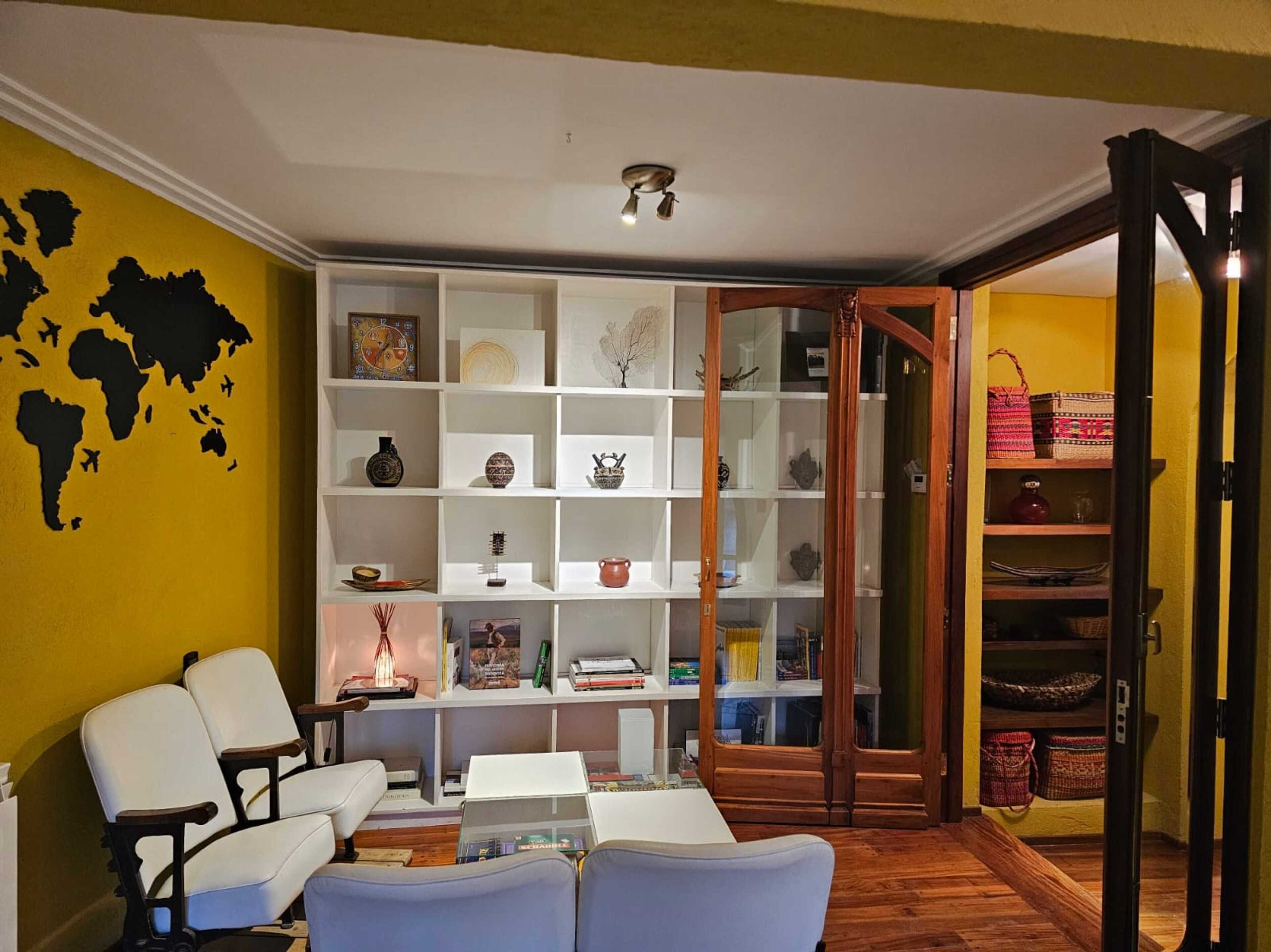 A living room with a bookshelf, two white chairs, a coffee table, and a world map on the wall.